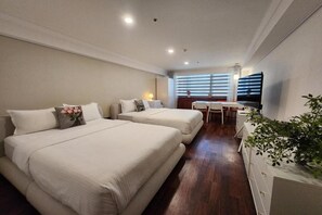 Una habitación de hotel con dos camas, un escritorio, una silla, un televisor y una planta.