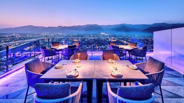 A rooftop dining area with tables and chairs, overlooking a cityscape and mountains. - Movenpick Hotel Centaurus (Islamabad)