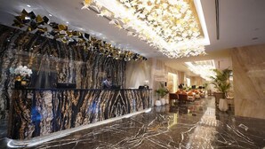 A hotel lobby with a marble reception desk, a chandelier, and a seating area with sofas. - Movenpick Hotel Centaurus (Islamabad)