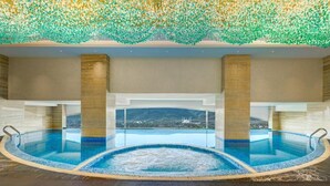A large indoor swimming pool with a clear view of a distant cityscape through the pool's edge. - Movenpick Hotel Centaurus (Islamabad)