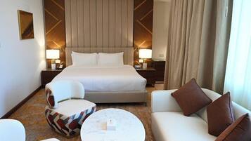 A hotel room with a large bed, two bedside tables with lamps, a sofa, a chair, and a coffee table.