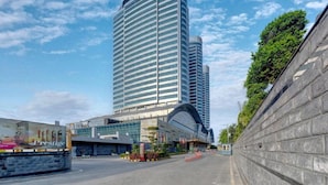 A modern hotel with a curved glass facade, a prominent entrance, and a stone retaining wall. - Movenpick Hotel Centaurus (Islamabad)