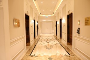 A hotel corridor with a marble floor, wall-mounted light fixtures, and a door at the end. - Westpac Hotel & Suites (Doha)