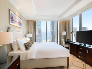 Ein Hotelzimmer mit einem großen Bett, einem Schreibtisch, einem Fernseher und Blick auf hohe Gebäude.
