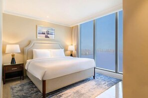 Habitación de hotel con una cama grande, dos lámparas de noche, un cuadro en la pared y vistas amplias por una ventana grande.
