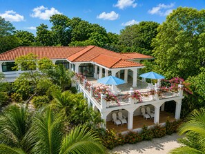 A two-story building with a red-tiled roof, white columns, and a covered outdoor seating area with umbrellas.