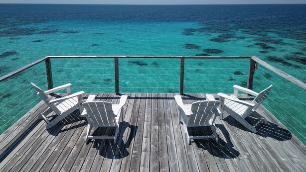 A wooden deck with white chairs overlooking turquoise ocean waters.
