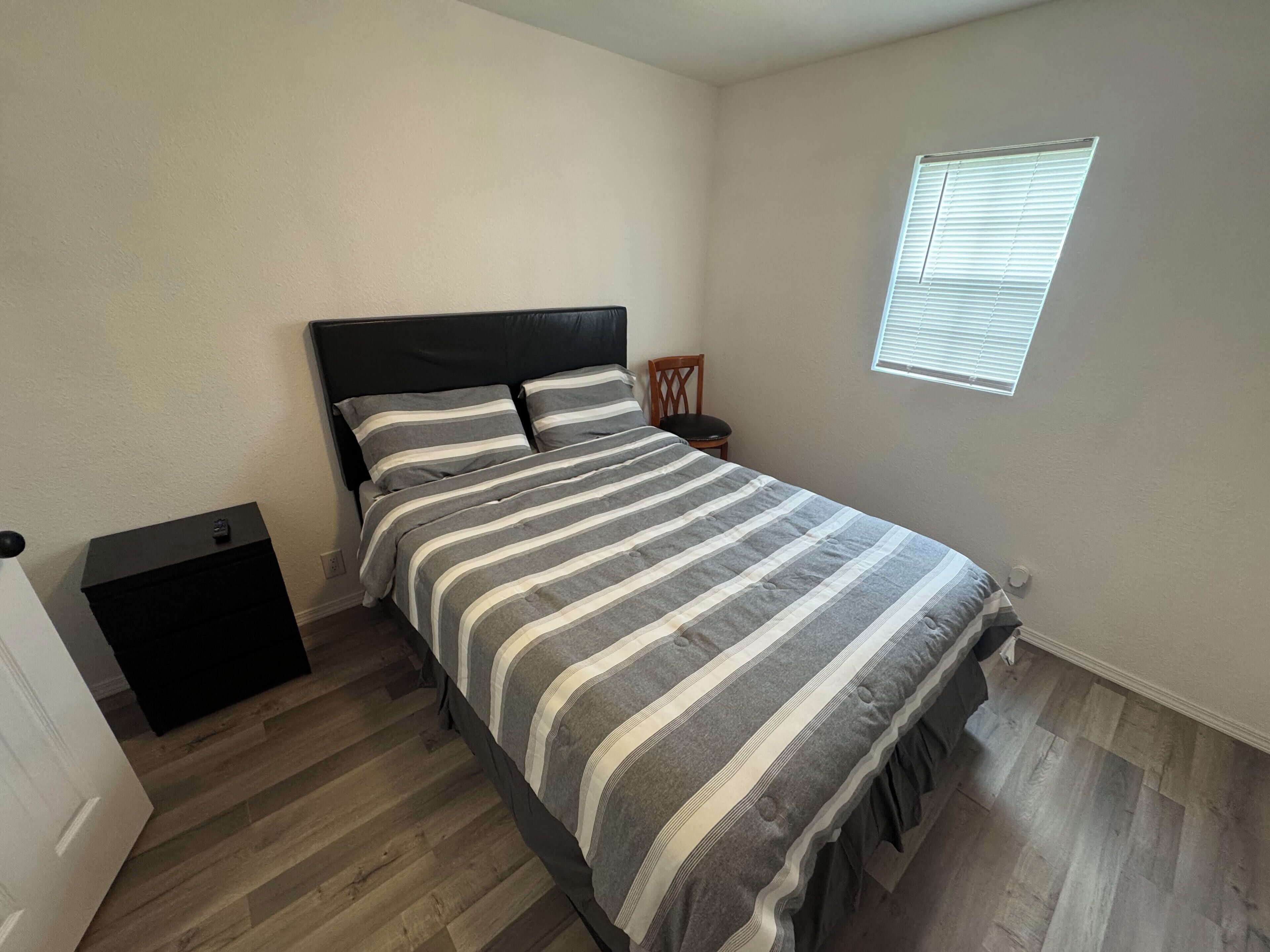 A bedroom with a bed, a nightstand, a chair, and a window.