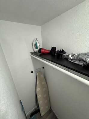 Un lavadero pequeño y ordenado con tabla de planchar, plancha y cepillo.