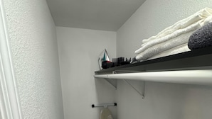 Kapea käytävä, jossa on kattoon kiinnitetty silityslauta, luuta ja moppi.