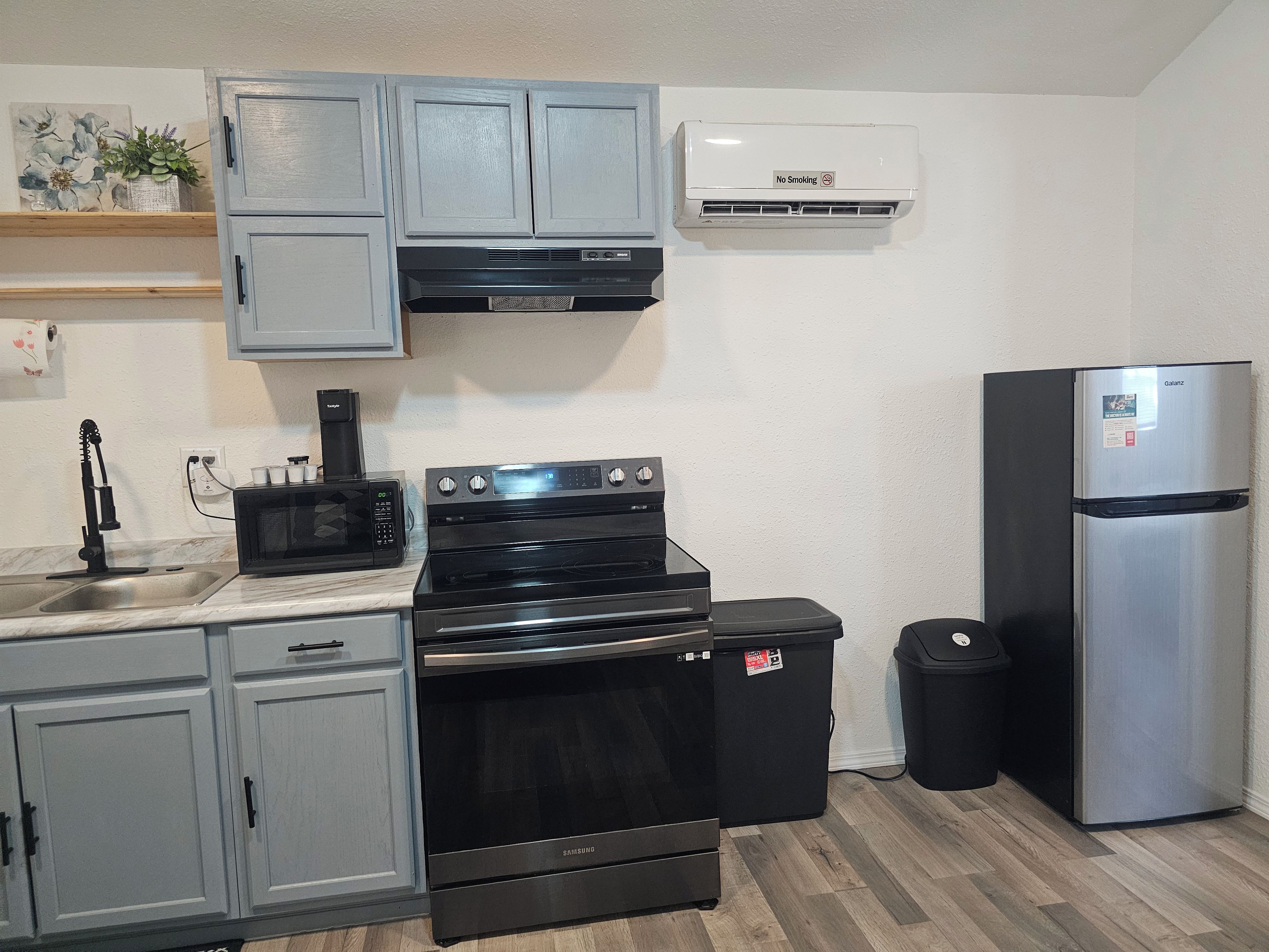 A kitchen with grey cabinets, a black stove, a microwave, a stainless steel refrigerator, and a wall-mounted air conditioner.