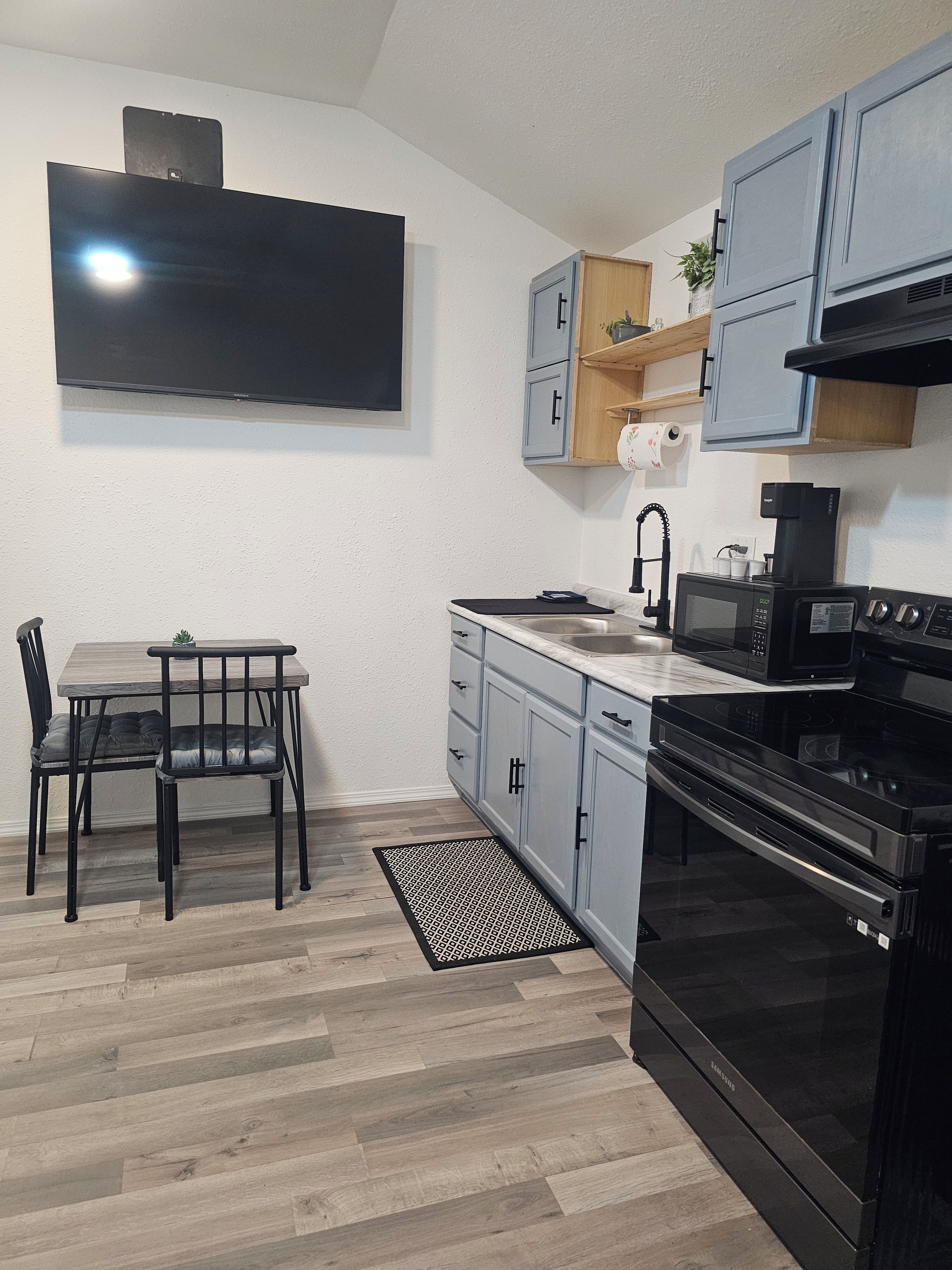 A modern kitchen with a flat-screen TV, a dining table with chairs, and a built-in oven.