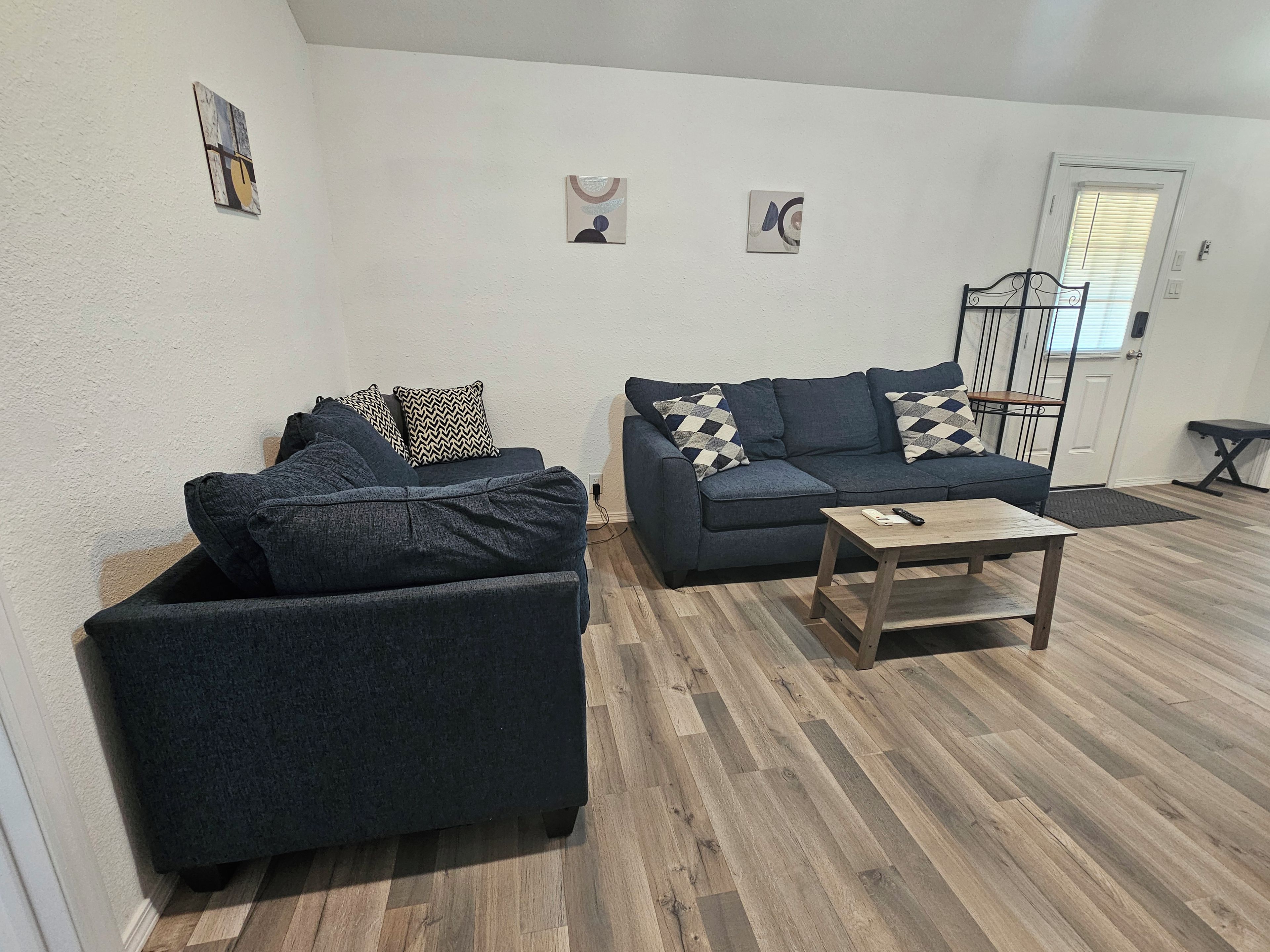 Una sala de estar con dos sofás oscuros, una mesa de centro de madera y una puerta con ventanal.