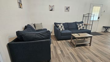 Una sala de estar con dos sofás oscuros, una mesa de centro de madera y una puerta con ventanal.