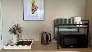 Una kitchenette con una obra de arte de una mariposa enmarcada, cafetera, microondas y un organizador escalonado para tazas.