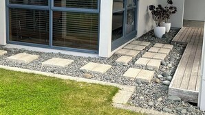 Un edificio moderno con ventanas amplias, un camino de piedra y una pequeña zona ajardinada.
