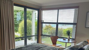 Un dormitorio con una cama grande, una puerta corrediza de vidrio a un balcón y una pequeña mesa con una planta.