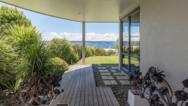 Un espacio al aire libre cubierto con piso de madera, plantas en macetas y vista al mar.