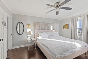 A bedroom with a bed, a nightstand, a ceiling fan, a mirror, and a window with curtains.