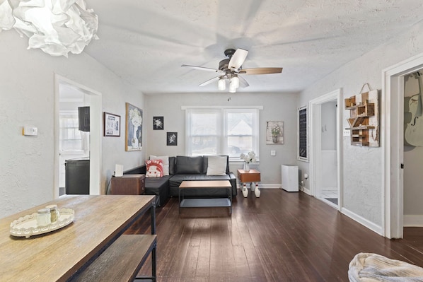 A living room with a sofa, a coffee table, a ceiling fan, and a dining area with a wooden table and chairs.
