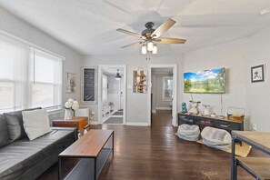 A living room with a sofa, a coffee table, a ceiling fan, a TV, and a painting on the wall.