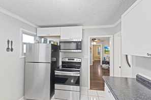 A kitchen with stainless steel appliances, white cabinets, and a view into the living area.
