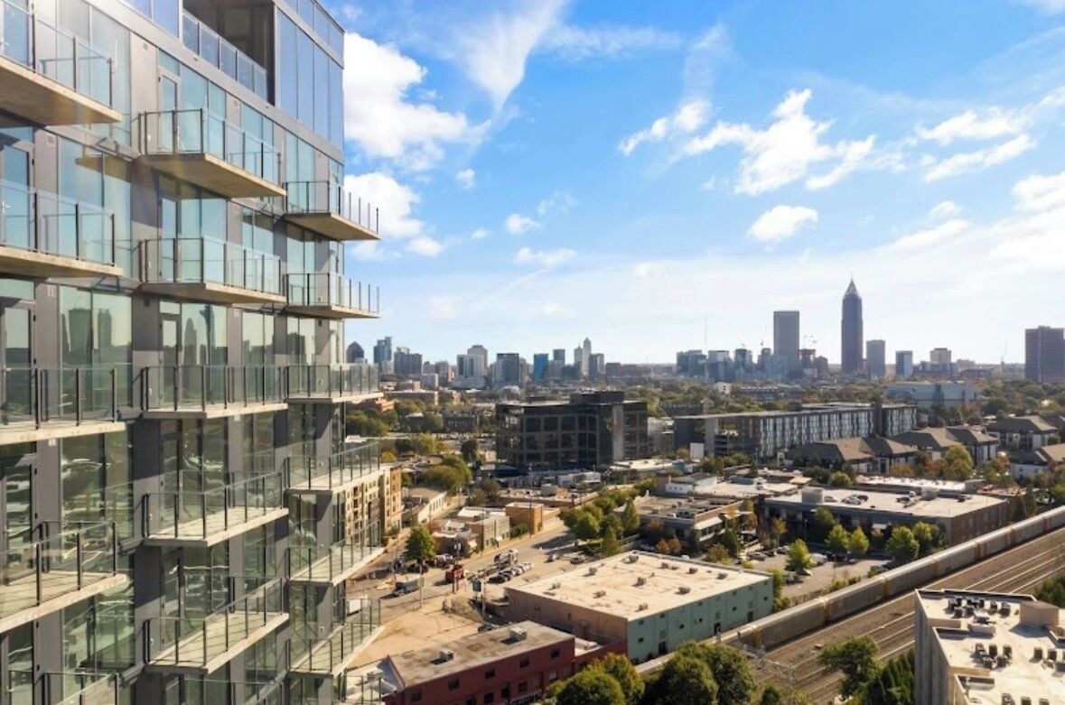 A modern high-rise building with a glass facade, a city skyline in the background, and a clear sky.