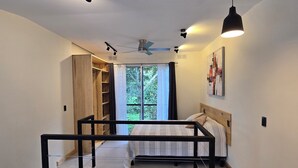 Ein Schlafzimmer mit einem Bett, einem Deckenventilator, einem Fenster mit Vorhängen, einer Holztreppe und einem Bild an der Wand.