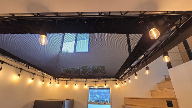 Ein Zimmer mit Deckenventilator, Lichterketten, einem großen Fenster und einer Holztreppe.
