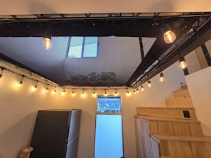 A room with a ceiling fan, string lights, a large window, and a wooden staircase. - New Cozy 1-bedroom apartment in Escazú for a relaxing stay & great location (Escazú)