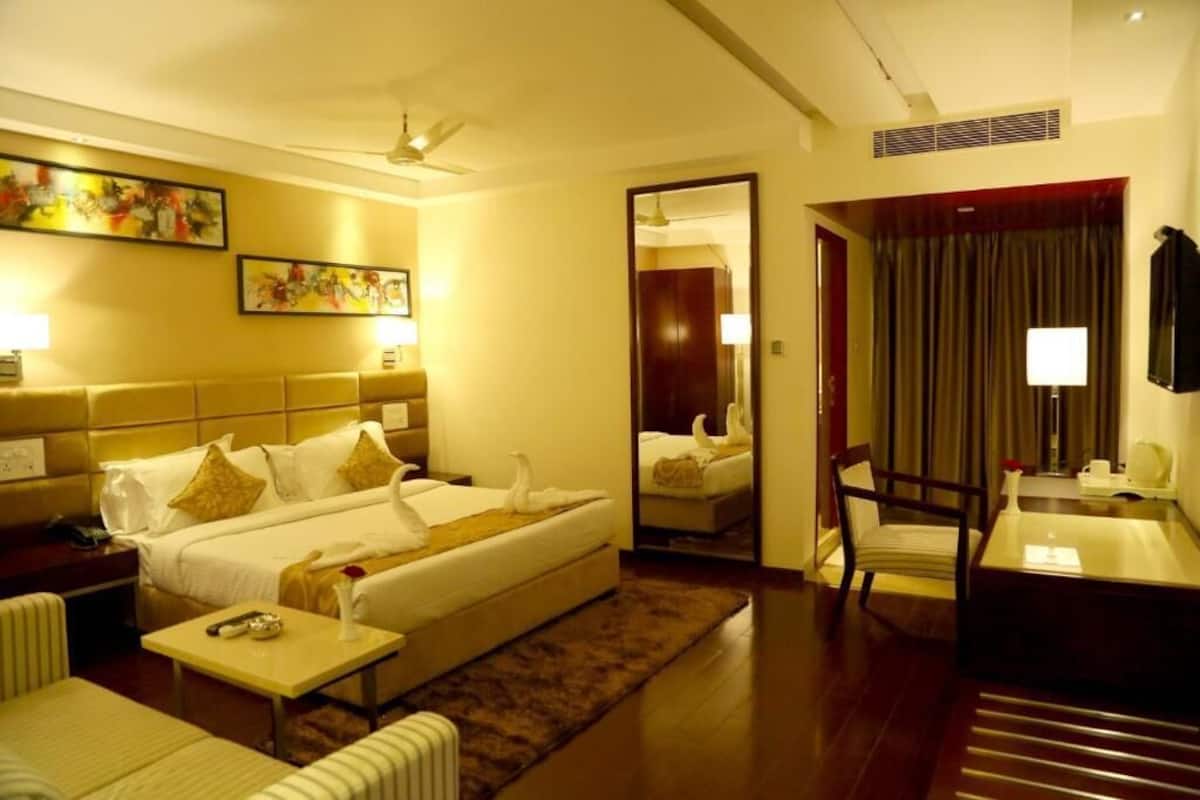 A hotel room with a bed, a desk, a chair, a mirror, and artwork on the walls.