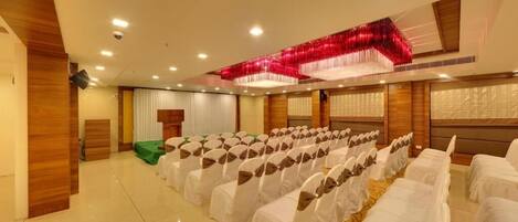 A conference room with rows of white chairs, a green carpet, and a red decorative element on the ceiling.