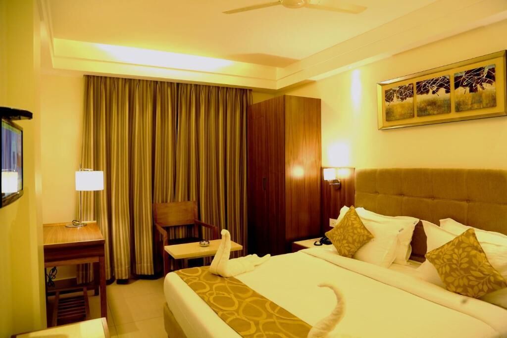 A hotel room with a bed, a desk, a chair, a lamp, a wall-mounted artwork, and a curtain.