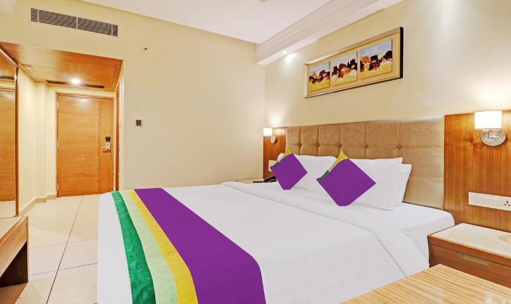 Camera d'albergo con un letto, comodini, testiera, un'opera d'arte appesa al muro e una porta.