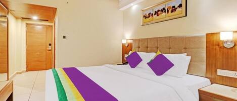 A hotel room with a bed, bedside tables, a headboard, a wall-mounted artwork, and a door.