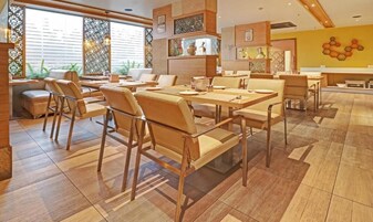 Un restaurante con mesas y sillas de madera, piso de baldosas y una pared de acento amarilla.