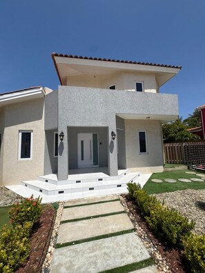 Ein modernes, zweistöckiges Haus mit Flachdach, einer Eingangstür mit Stufen und einem kleinen Balkon im Obergeschoss.