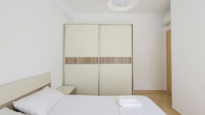 A bedroom with a bed, a nightstand, a wardrobe, and a ceiling light. - Lura Apartment 05 in Plazhi San Pietro (Ishëm)