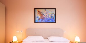 Ein Hotelzimmer mit einem Bett, zwei Nachttischlampen und einem farbenfrohen, abstrakten Gemälde an der Wand.
