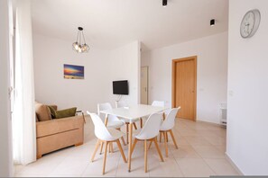 A modern living room with a white sofa, a dining table with chairs, a flat-screen TV, and a painting on the wall. - Lura Apartment 06 in Plazhi San Pietro (Ishëm)