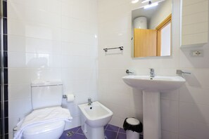 A bathroom with a toilet, bidet, sink, mirror, and a trash bin. - Lura Apartment 06 in Plazhi San Pietro (Ishëm)