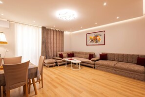 A modern living room with a sectional sofa, a dining table with chairs, and a small white table. - Ground-floor Apartment Private Garden (Ishëm)