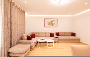A modern living room with a sectional sofa, a small coffee table, and a framed artwork on the wall. - Ground-floor Apartment Private Garden (Ishëm)