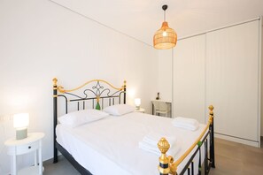 A neatly made bed with white linens, a bedside table with a lamp, and a hanging light fixture. - Boho-chic Apartment With Garden Views (Ishëm)
