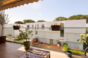 Ein Balkon mit Blumentöpfen, einem Tisch und Blick auf einen modernen Gebäudekomplex.