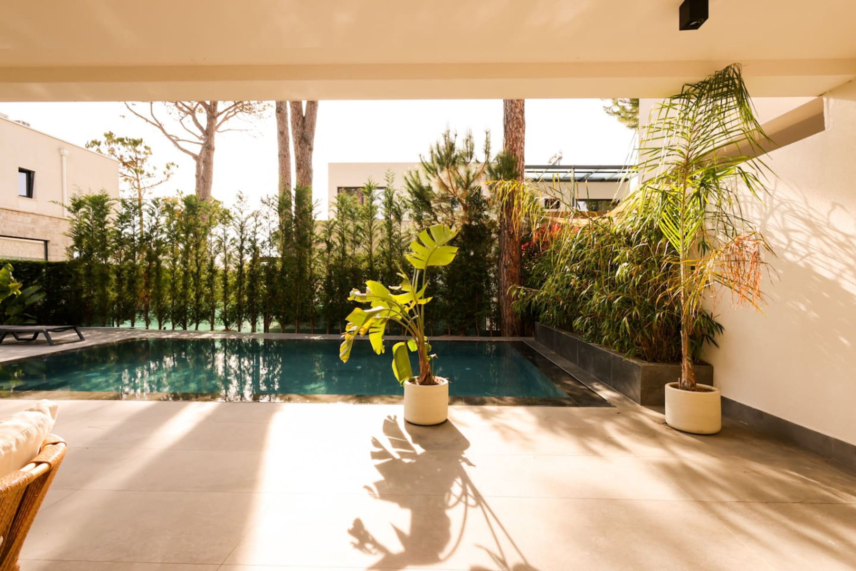 A poolside area with a lounge chair, potted plants, and a view of a swimming pool.