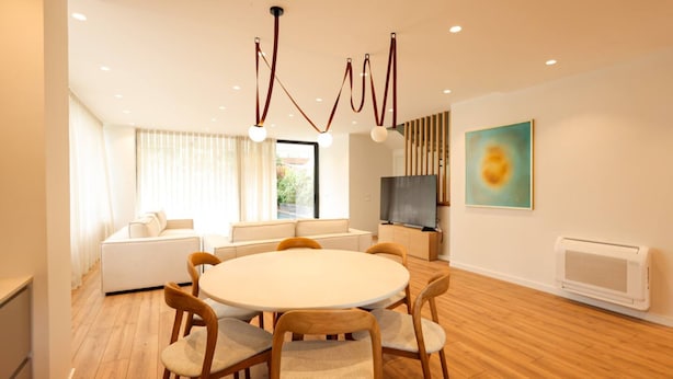 Una sala de estar moderna con una mesa redonda, sillas de madera, un sofá, un televisor y un cuadro en la pared.