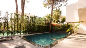 Una piscina con un deck perimetral, árboles y una hamaca.
