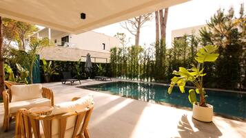 A poolside area with wicker furniture, a potted plant, and a view of a building in the background.
