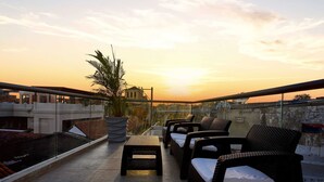 Une terrasse sur le toit, aménagée avec du mobilier d’extérieur, un grand pot de fleurs et offrant une vue sur le coucher de soleil.